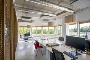 Modern kantoorinterieur aan de Anthony Fokkerweg met ruime werkplekken en grote ramen die uitzicht bieden op groen en een snelweg.